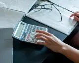 Ręce liczą na kalkulatorze dokumenty, analizując umowę zlecenie a alimenty. Obok leżą okulary i notatki.