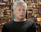 Un uomo con capelli grigi davanti a uno sfondo di libri antichi, forse ispirato ai libri di Alessandro Baricco.