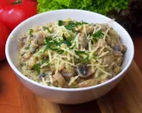 Pyszne risotto z pieczarkami, posypane startym serem i świeżą natką pietruszki, czeka w białej miseczce.