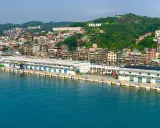 Vista panoramica del porto di Taiwan, con edifici colorati che si arrampicano sulla collina verde. La scritta "KEELUNG" domina la cima.