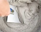 Maintenant, vous savez comment faire du ciment. Une main utilise une truelle pour mélanger la pâte grise dans un seau.