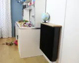 Un radiateur Qarnot particulier noir, surmonté d'un plateau en bois et d'un globe, réchauffe la chambre d'enfant remplie de jouets.