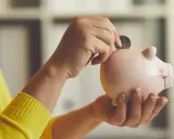 Manos introducen una moneda en una hucha rosa, simbolizando el ahorro para recuperar plan de pensiones nueva ley.