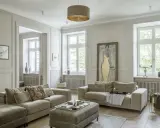 Elegancki salon z dwoma beżowymi sofami, ozdobną sztukaterią na ścianach i dużym obrazem.