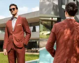 Man in a rust-colored suit, perfect semi formal attire for a wedding. He wears sunglasses and a light shirt, looking dapper outdoors.