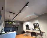 Nowoczesne oświetlenie w salonie fryzjerskim tworzy przytulną atmosferę. Reflektory na szynach i wisząca lampa z zielenią podkreślają styl wnętrza.