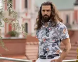 Mężczyzna z długimi włosami w hawajskiej koszuli na t-shirt, z motywem liści i ptaków.
