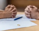 Złożone dłonie nad dokumentami, na stole leży obrączka. Czas na decyzję o zmianie nazwiska rodowego.