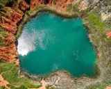 Lago turchese circondato da rocce rosse e vegetazione rigogliosa, un paesaggio suggestivo che ricorda le cave di bauxite.
