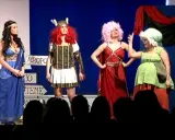 Attrici in costume su un palco, forse per la lisistrata trama. Una in blu, una guerriera, una con capelli rosa e una in verde.