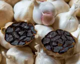 Deux têtes d'ail noir coupées en deux, révélant leur intérieur caramélisé, reposent sur un lit d'ail blanc frais. Parfait pour une recette d'ail noir.