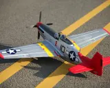 Ein detailgetreues Modell eines Mustang-Flugzeugs mit roten und silbernen Akzenten steht auf asphaltiertem Untergrund mit gelben Markierungen.