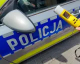 Policjantka trzyma alkomat przy radiowozie. Wynik 13.7 promila to nierealny, ale symboliczny wynik dla kierowcy pod wpływem alkoholu.
