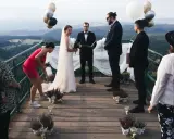 Niezwykły ślub w górach. Para młoda, urzędnik i goście na tarasie z widokiem na dolinę. Balony unoszą się w powietrzu.