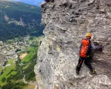 Wspinaczka via ferrata w Szwajcarii. Widok na dolinę i miasteczko z perspektywy skalnej ściany.