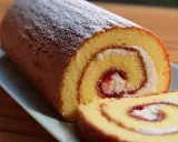 En saftig glutenfri rulltårta med sylt och grädde, pudrad med florsocker.