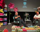 Jan Guillou delar fakta på Rinkeby Bokfestival. Scenen är dekorerad med stora blommor och bokhyllor.