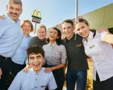 Uśmiechnięty zespół McDonald's, gotowy do pracy. W tle logo McCafe.
