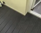 Ciemnoszara deska kompozytowa pełna, tworząca nowoczesną podłogę tarasu, z widocznym fragmentem drzwi balkonowych i jasną ścianą.