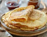 En hög med gyllene tunna pannkakor, pudrade med florsocker, redo att avnjutas med sylt och honung.