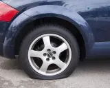 Ruota posteriore di un'auto blu con evidente perdita pressione pneumatici. Il pneumatico è sgonfio e appoggiato a terra.