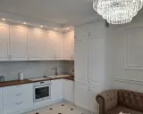Elegancka kuchnia w stylu angielskim z białymi frontami, drewnianym blatem i kryształowym żyrandolem.
