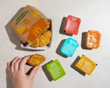 Ręka sięga po McNuggeta z pudełka. Obok sosy: Tangy BBQ, Spicy Buffalo, Ranch, Sweet 'N Sour, Honey Mustard. 20 McNuggets kcal to kusząca wizja.