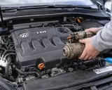 Ręce trzymają zużyty rozrusznik, gdy samochód nie chce odpalić. Widoczny silnik TDI Volkswagena.
