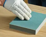 Ręka w białej rękawiczce testuje, jaki papier ścierny do drewna będzie najlepszy.