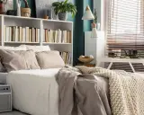 Una cama acogedora con una estantería encima llena de libros y plantas.
