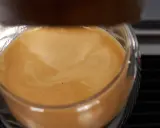 Ein Glas mit cremigem Kaffee, das ist cafe crema mit milch. Die goldbraune Crema wirbelt sanft.
