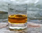 Ein Glas goldener Whisky steht auf einem Stein am Flussufer. Die ideale trinktemperatur für diesen edlen Tropfen.