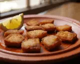 Deliciosos trozos de bacalao rebozado, dorados y crujientes, servidos en un plato de barro con una rodaja de limón.