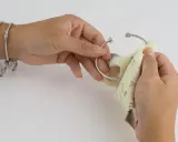 Manos puliendo un brazalete de plata con un paño. Aprende como limpiar cadena de plata y mantener tus joyas brillantes.