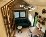 Przytulne wnętrze tiny house Polska: zielona kanapa, drewniane meble i nowoczesne oświetlenie. Idealne miejsce na relaks.
