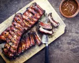 Soczyste żeberka w miodzie, grillowane do perfekcji, leżą na desce obok sosu.
