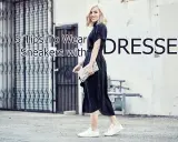 A woman shows how to wear sneakers with a dress, pairing white sneakers with a black midi dress and a clutch.
