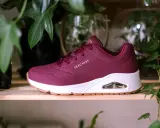 Bordowy but Skechers z białym spodem i brązową podeszwą, otoczony zielonymi liśćmi. Dowiedz się, jak wyczyścić sznurówki, aby buty wyglądały jak nowe.