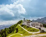 Un borgo incantevole in montagna, perfetto per le tue vacanze in Friuli. Case bianche, una chiesa e sentieri verdi sotto un cielo nuvoloso.