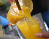 Ein Mann gießt leuchtend gelben Saft, vielleicht Poncha Madeira, aus einer Glaskaraffe in zwei Gläser mit Eiswürfeln.