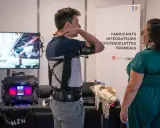 Un homme teste un exosquelette pour le bras, une technologie d'assistance pour le handicap. Une femme observe.