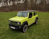 Jaskrawozielony Suzuki Jimny 5-drzwiowy na trawie. Sprawdź jego cenę i możliwości terenowe!