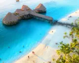 Zanzibar w czerwcu: idealna pogoda na wypoczynek na rajskiej plaży z turkusową wodą i palmami. Widać hotel na wodzie i ludzi kąpiących się.
