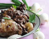 Un plat de coq au vin savoureux, avec des morceaux de poulet tendres, des champignons et des oignons dans une sauce riche.