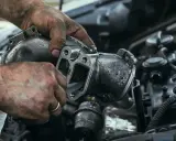Brudne ręce mechanika czyszczą zapieczony zawór EGR. Widać narzędzie wsuwane do wnętrza elementu.