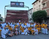 Grupo posa en la fiesta longaniza Graus, con un cartel de "Los Tres Sabores de la Longaniza de Graus" y una estructura de madera con embutidos.