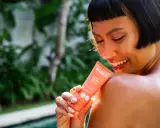 Une femme souriante applique une crème solaire SPF 50+ sur son épaule. Le tube indique "Très haute protection", le SPF 50 signification est une protection optimale.