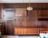 En väggmonterad hylla i teak, troligen designad av Poul Cadovius, med glasmonter, lådor och hyllplan.
