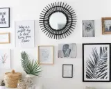 Un mur de cadres éclectique avec un miroir soleil, des photos et des citations inspirantes.