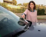 Mujer saca papel del parabrisas, preocupada por como saber si me han multado.